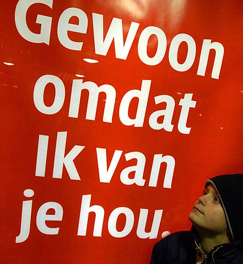 Jongetje leest tekst van reclameposter op NS-station. ,,Gewoon omdat ik van je hou'' staat er in witte letter op een knalrode achtergrond. En de verwijzing dat je snel op www.waaromkerst.nl moet kijken voor de achterliggende reden van deze reclame-uiting.