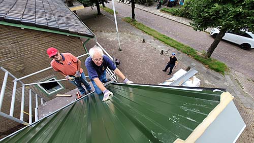 Verbouw schuur Doarpskeamer Akkrum-NesDe schuur naast de Doarpskeamer Akkrum-Nes is tijdens de zomermaanden ingrijpend verbouwd. De ruimte wordt geschikt gemaakt voor activiteiten, zoals timmer- en schilderscursussen en bloemschikken. Een ploeg vrijwilligers heeft in wisselende samenstelling de klus geklaard.Het grotendeels vrijstaande gebouw is straks volledig geïsoleerd. Vloeren en wanden zijn van isolatieplaten voorzien en met hout afgetimmerd. Geïsoleerde dakplaten zijn in twee dagen tijd gelegd. Het aftimmeren vindt de komende maanden plaats. Coördinator Roland van der Starre heeft in de afgelopen maanden heel wat werk verzet om de vrijwilligersploeg op sterkte te houden. Zelfs in zijn tennistrainingsploegje ronselde hij helpers. Wim Wouters, Fred Zondervan, Aize Wijnstra hebben onder andere de vloer en de wanden geïsoleerd en van nieuwe beplating voorzien.Het bouwteam kreeg vanwege de corona ook te maken met stijgende kosten voor materiaal en kampte met een soms problematische levering ervan. Harde wind zorgde ook een paar keer voor uitstel van het monteren van de dakplaten. De verbouw zorgde niet alleen voor uitgaven, maar ook inkomsten: de oude dakplaten werden op Marktplaats verkocht. Asbestplaten achter de schuur zijn op zorgvuldige wijze weggehaald en naar het gemeentelijk stort gebracht. Op de foto Fred Zondervan (l) en Roland van der Starre, terwijl Eelco Sixma klaar staat voor hand- en spandiensten.